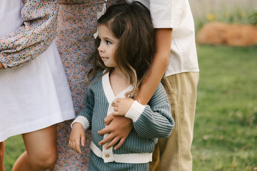A child is held by one of her siblings so she won't walk away during their family session on Oahu
