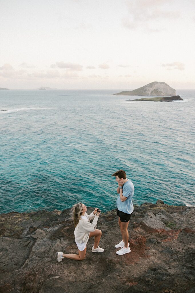 After being proposed to a woman flips the roles and proposes to her now fiancé who acts shocked, they're standing atop Makapuu Lookout which looks out over the ocean and other Hawaiian islands