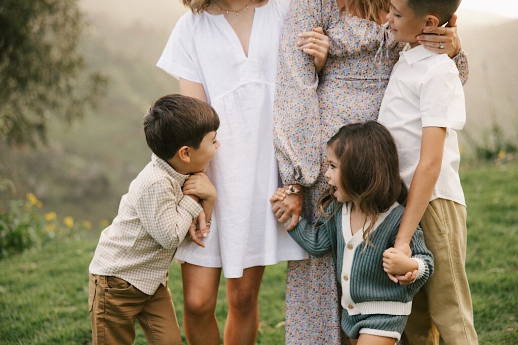 Four children stand around their mother during a family session on Oahu, the 2 youngest children are laughing at one another