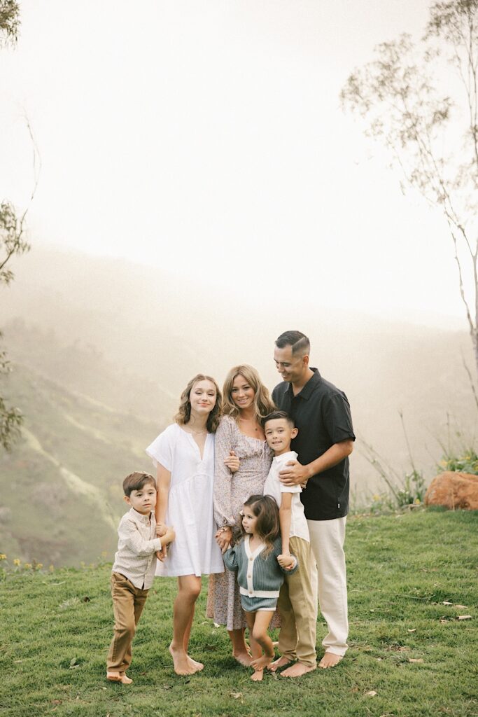 A family stand together and pose for a photo with the foggy mountains of Oahu behind them