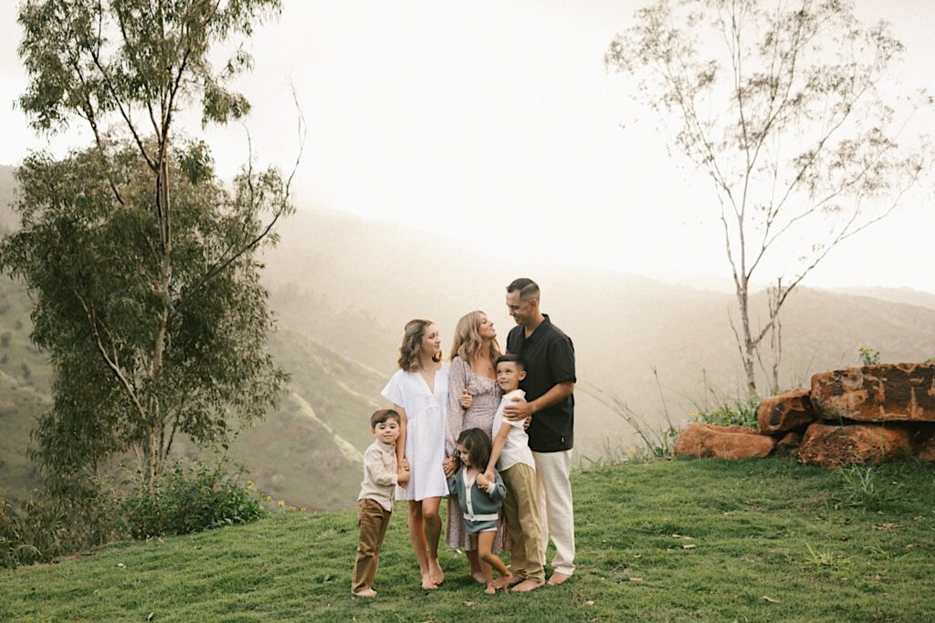 A family stand together and pose during their family session with the foggy mountains of Oahu behind them