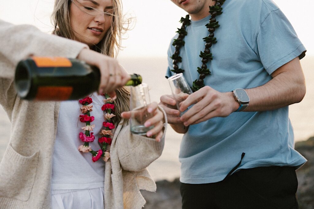 After their proposal on Makapuu Lookout in Hawaii a couple pour champagne in glasses to celebrate their engagement