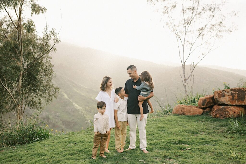 A father stands with his four children during their family session on Oahu with foggy mountains behind them