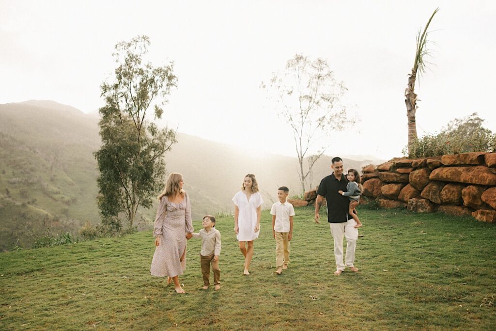 A couple and their four children walk towards the camera during their family session on Oahu with foggy mountains behind them