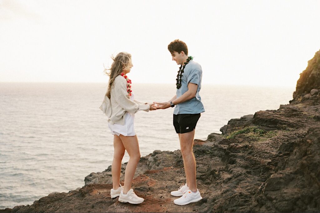 A couple hold hands and look at one another while on Makapuu Lookout in Hawaii after their proposal