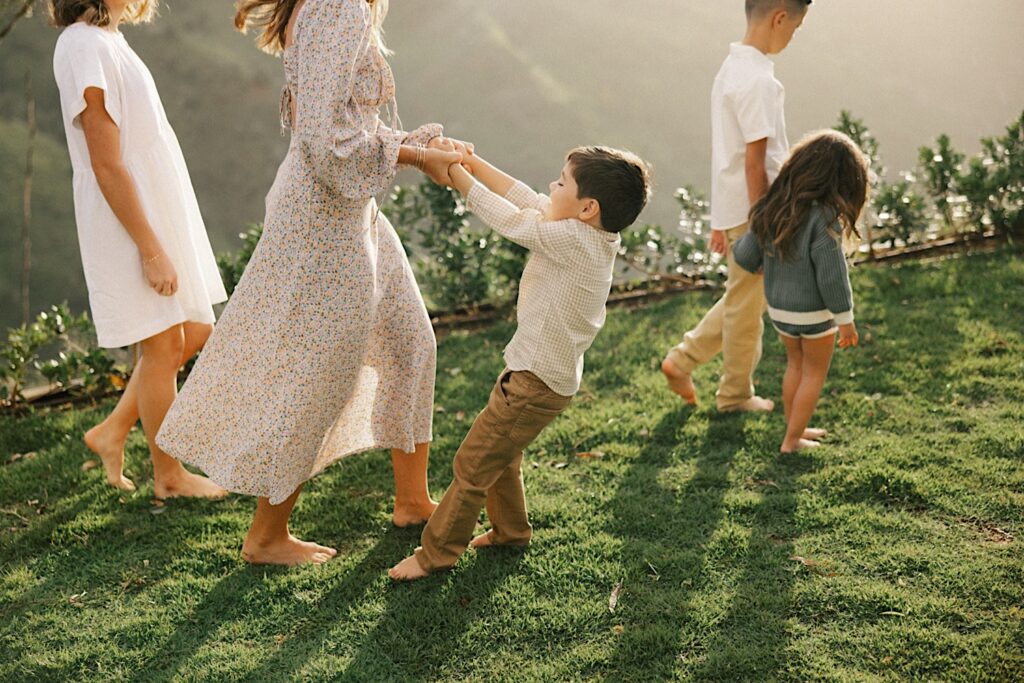 A child holds his mothers hands and swings while his 3 siblings walk alongside them during their family session on Oahu