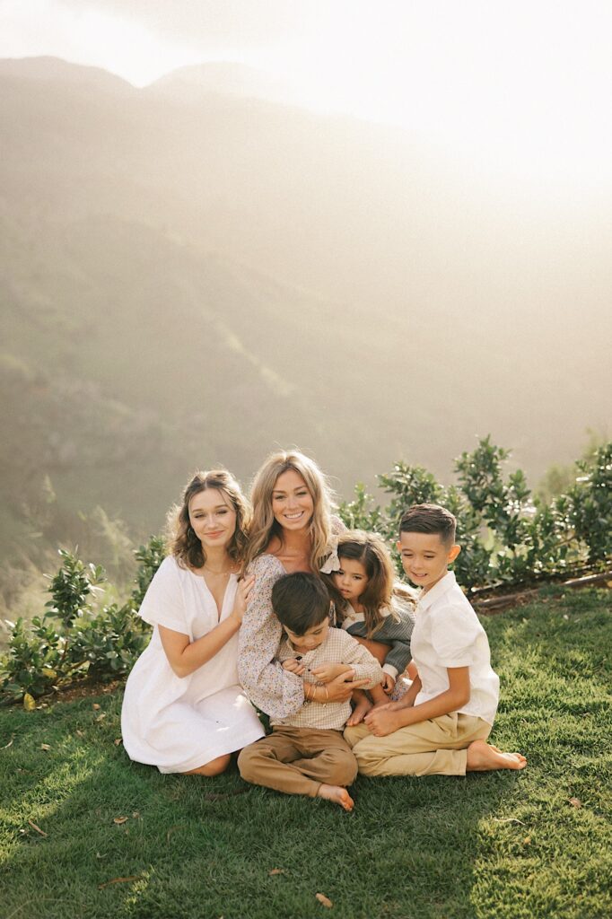 A woman sits on a cliff looking out over a mountain of Oahu surrounded by her 4 children
