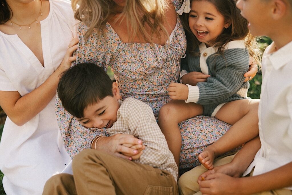 A group of 4 children surround their mom and laugh as they're tickled during their family session on Oahu
