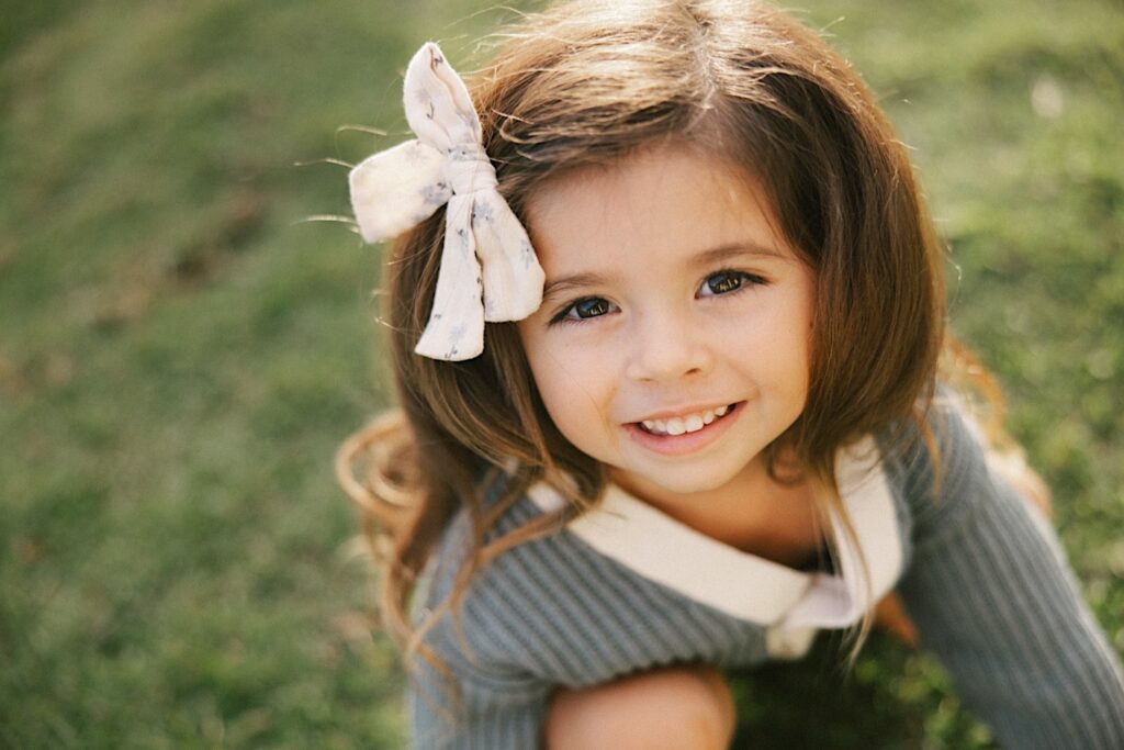 A young girl sits in the grass and smiles at the camera
