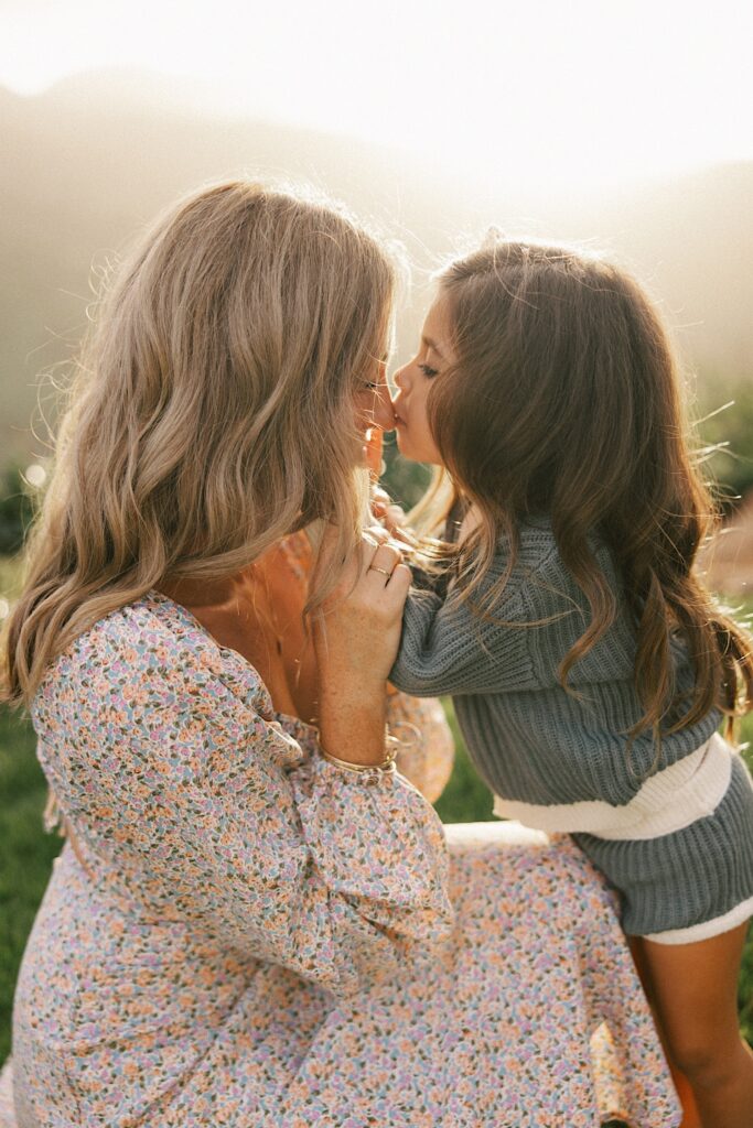 A woman gets a kiss on the nose from her youngest daughter while the sun rises over a mountain behind them