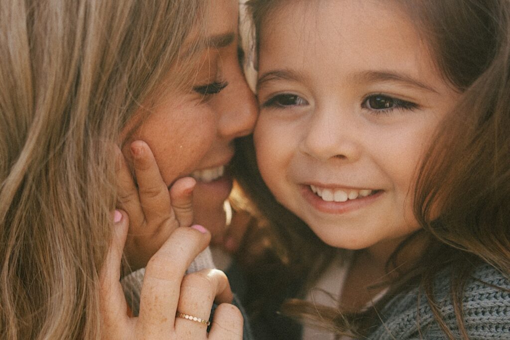 A mother presses her nose against her youngest daughter's cheek as she smiles.