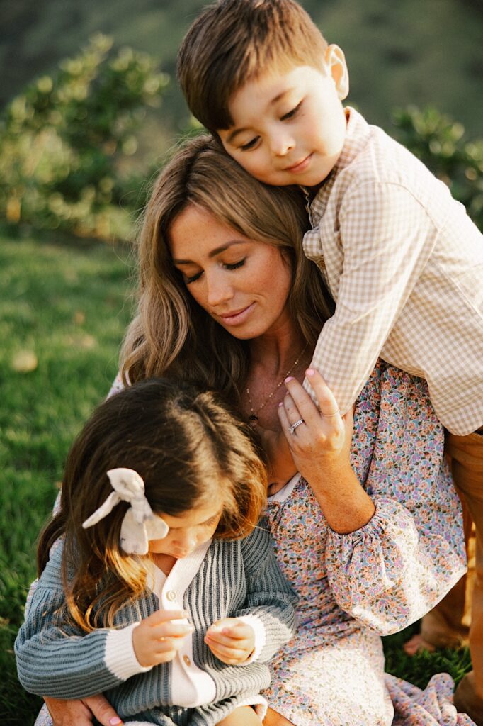 A mother holds her youngest daughter as her youngest sun hugs her from behind