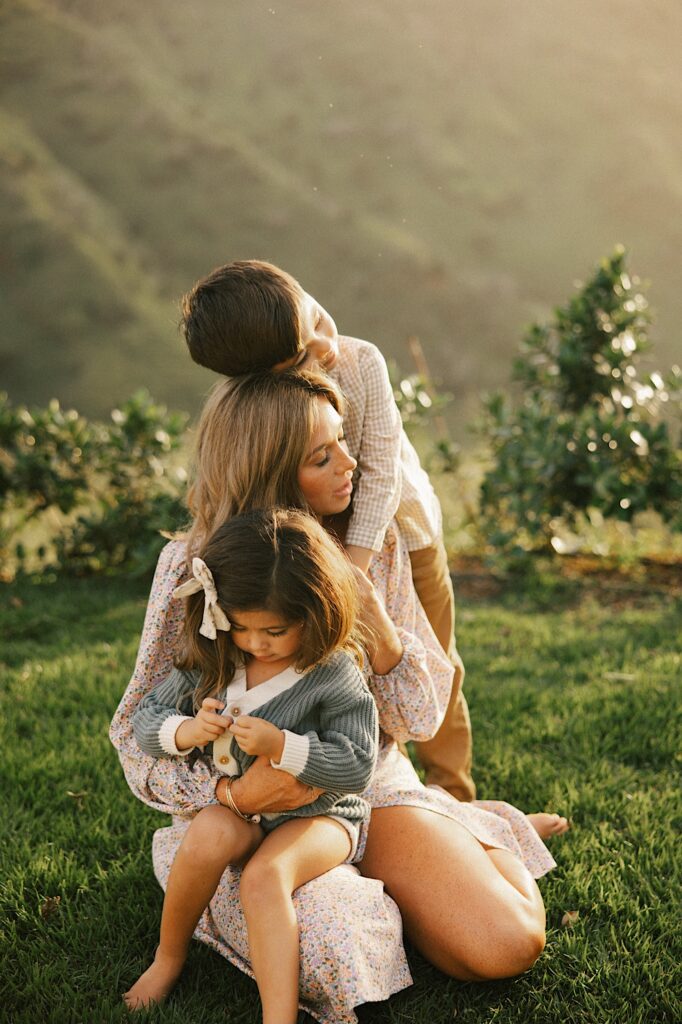 A mother holds her youngest daughter as her youngest sun hugs her from behind with the mountains in the background