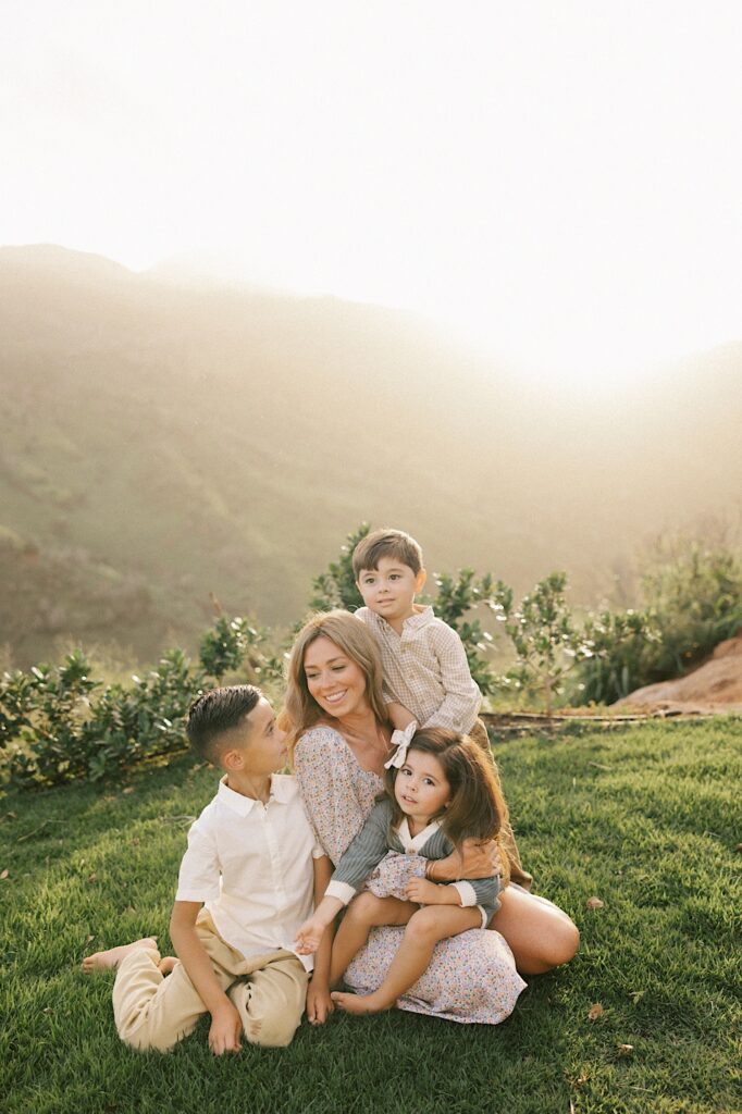 A mother sits surrounded by her three youngest children and smiles with them while the sun rises over the mountains of Oahu behind them