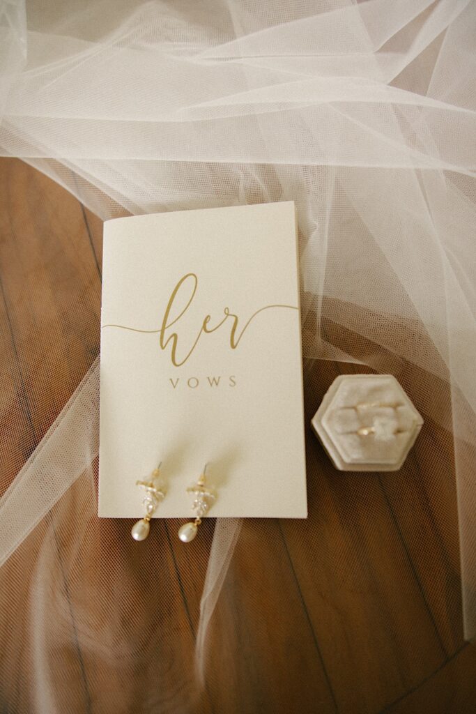 Detail photos of a book that reads "her vows" with earrings resting on it and clear white fabric underneath it