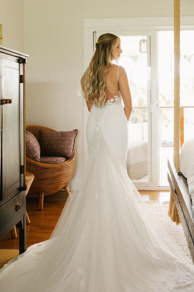 A bride stands facing away from the camera in her wedding dress and looks right over her shoulder