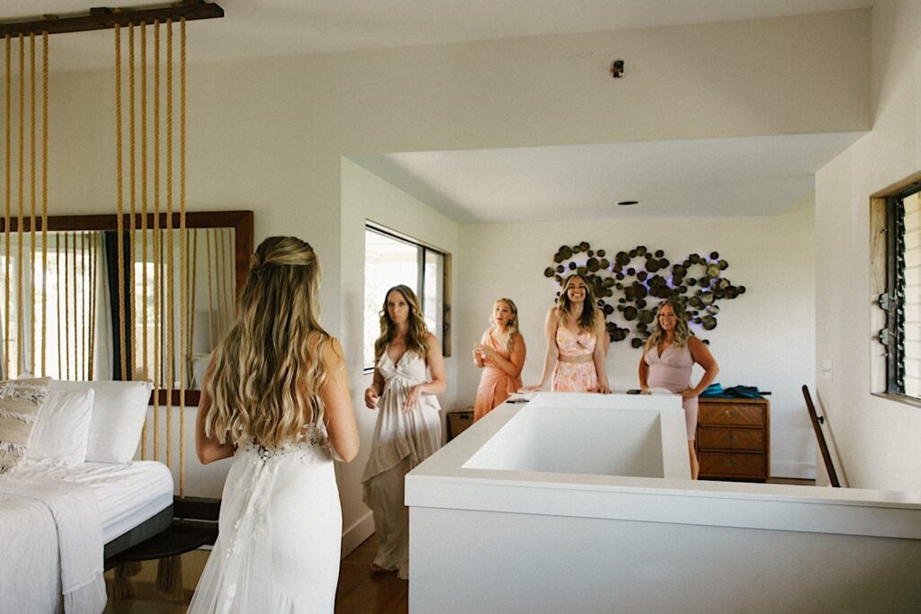 A bride stands in front of her 4 bridesmaids while wearing her wedding dress, the bridesmaids react with excitement seeing her for the first time