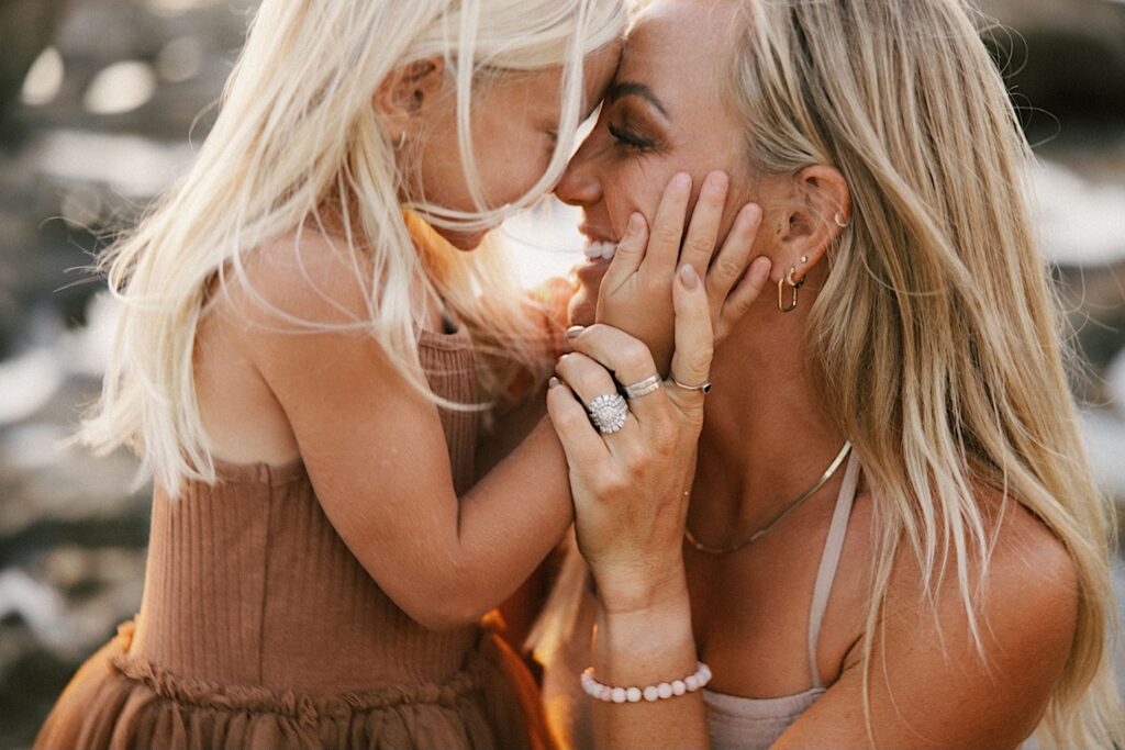 A mother and daughter smile as they touch noses together on the beach during their family session in Hawaii