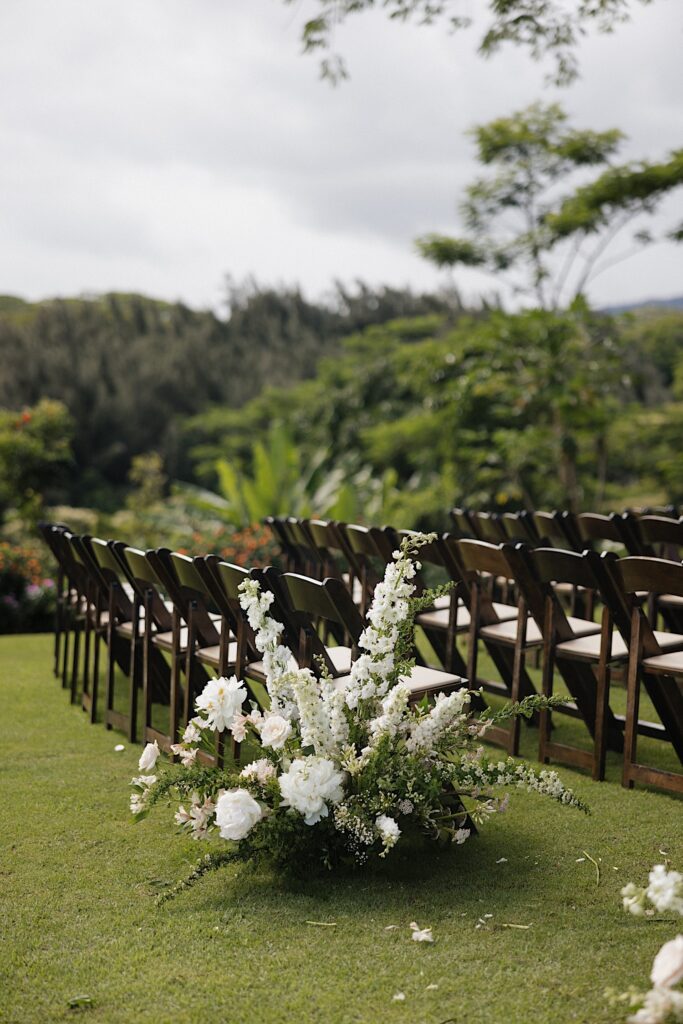 White flowers sit next to a row of wooden chairs set up for a wedding ceremony