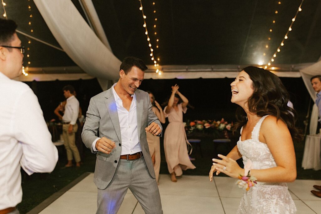 A bride and groom dancing underneath the tent with their wedding guests at their venue Lanikuhonua  on Oahu