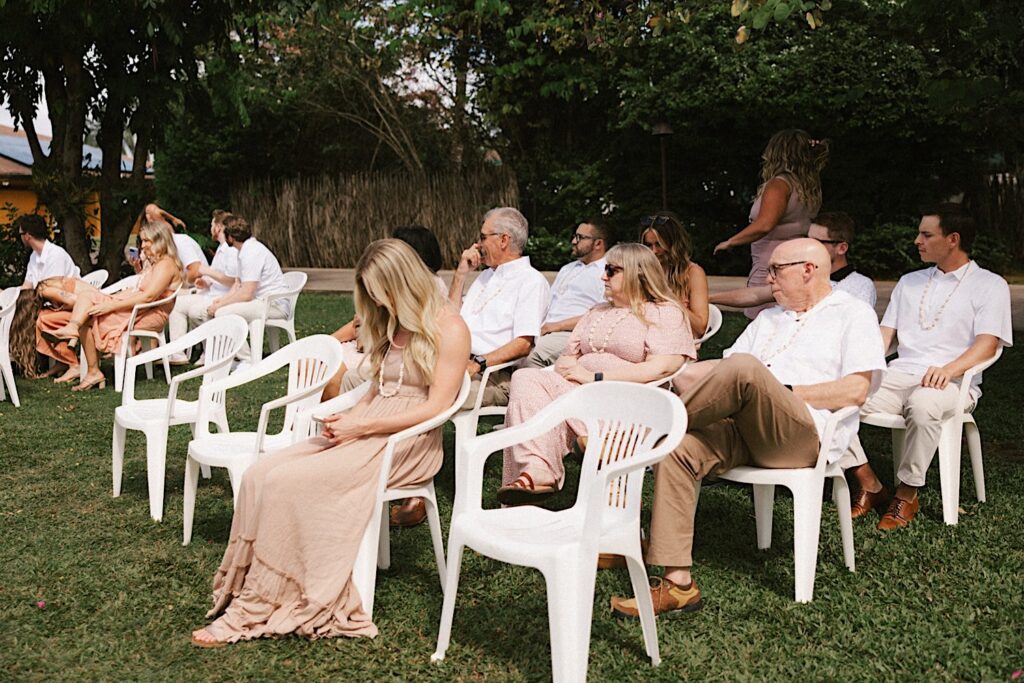 Guests of an intimate wedding on Kauai sit in white lawn chairs as they get ready for the ceremony to begin