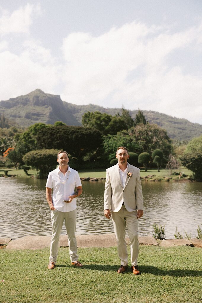 A groom and the officiant of a wedding stand together in front of a lake as the wedding ceremony is about to begin