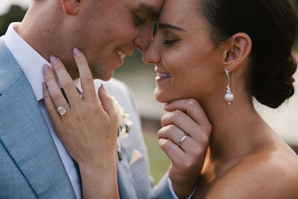 After their wedding ceremony at Kukui'ula on Kauai a bride and groom touch their noses together and smile with their wedding rings on full display with their hands touching one another's faces