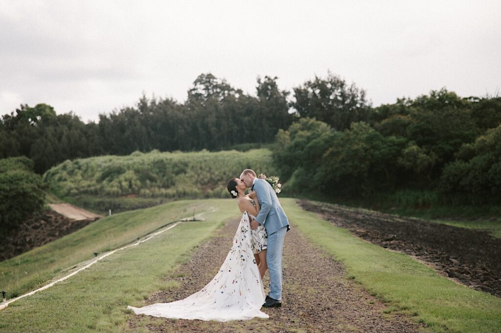 After their wedding ceremony at Kukui'ula on Kauai a bride and groom kiss one another while standing on a dirt path