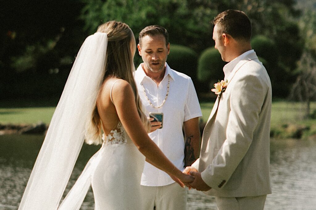 An officiant speaks while a bride and groom stand in front of him and hold hands during their intimate wedding on Kauai