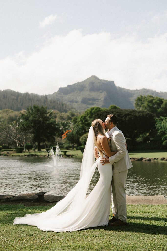 A bride and groom kiss one another during their wedding ceremony in front of a lake and a mountain in Hawaii