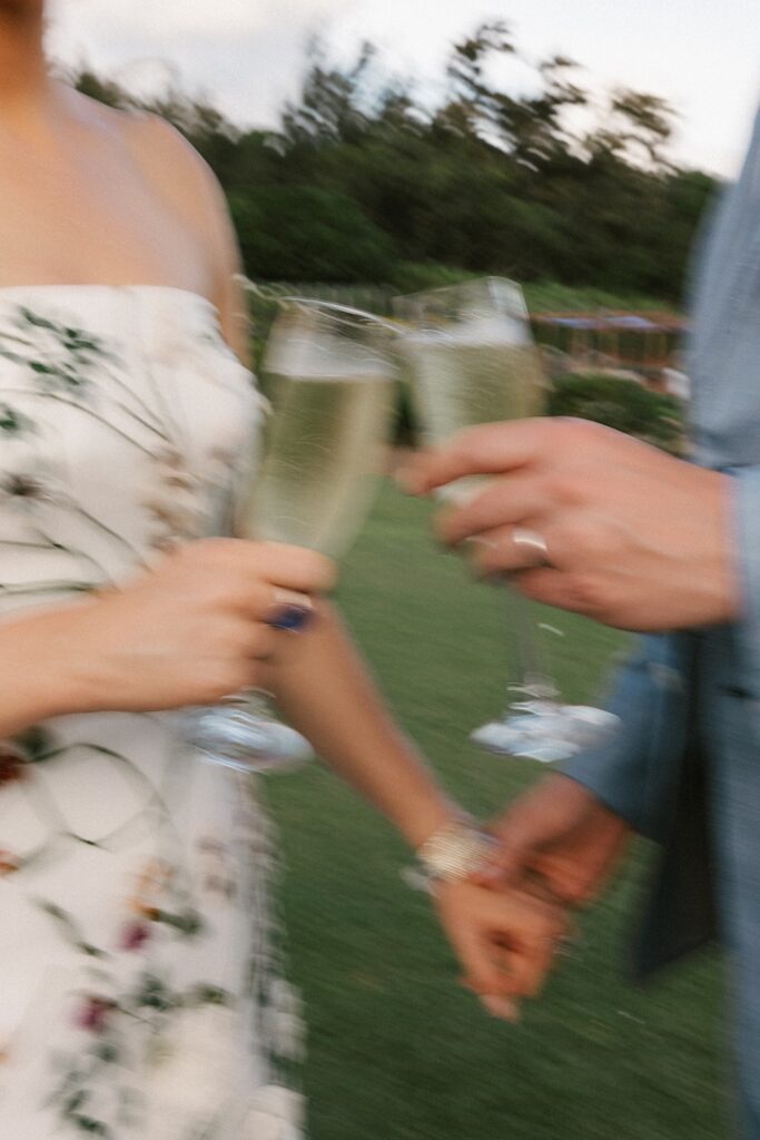 A blurry close up photo of a bride and groom's hands with champagne glasses  in either hand