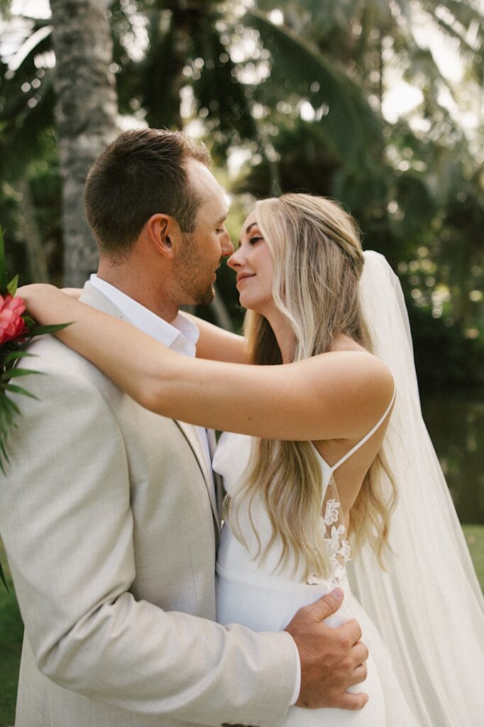 A bride and groom embrace and are about to kiss one another with palm trees behind them