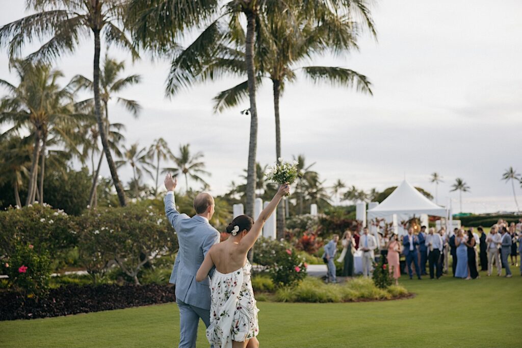 A bride and groom raise their hands as they walk towards the guests of their wedding reception at Kukui'ula on Kauai