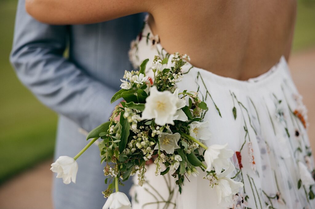 Close up photo of a bouquet of flowers, in the background are the bride and groom who are hugging one another