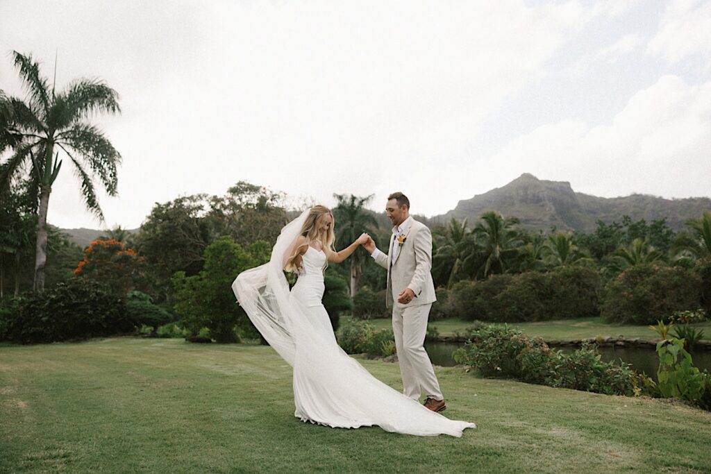 A bride and groom dance with one another in front of a river, palm trees, and a mountain after their intimate wedding ceremony on Kauai
