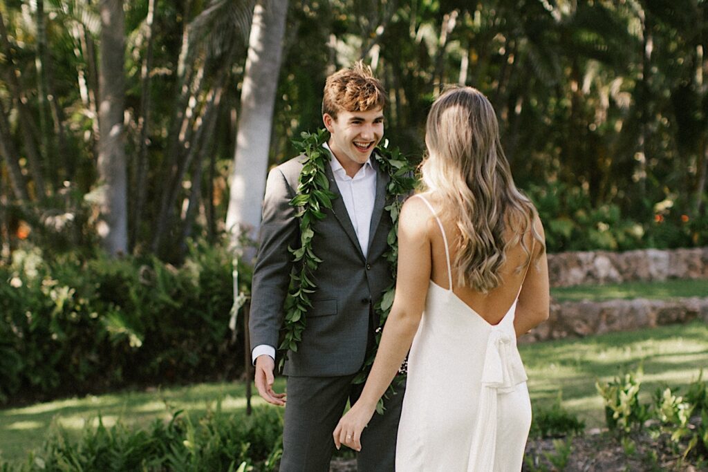During their Elopement at Lanikūhonua Oahu a groom exclaims with excitement as he sees the bride for the first time with palm trees in the background