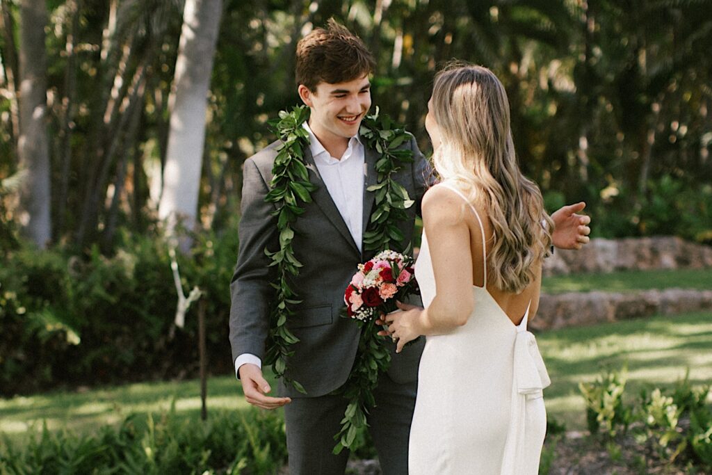 During their Elopement at Lanikūhonua Oahu a groom exclaims with excitement as he sees the bride for the first time with palm trees in the background