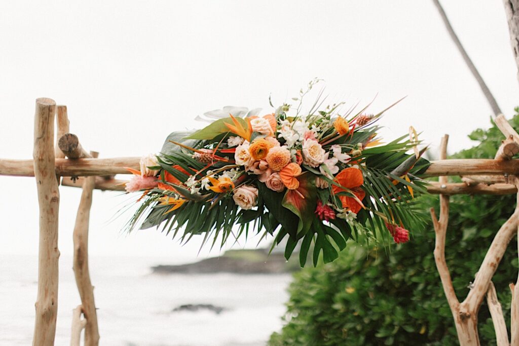 Wedding florals are attached to a wooden archway of a wedding ceremony
