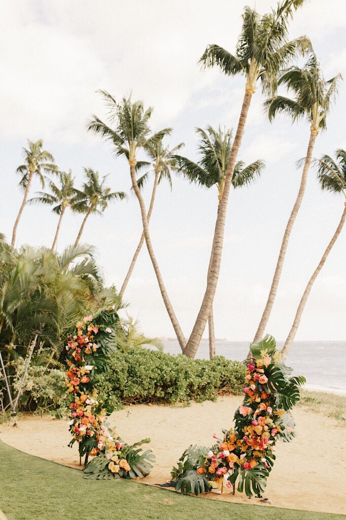 A ceremony space with a floral archway, palm trees, and the ocean behind it