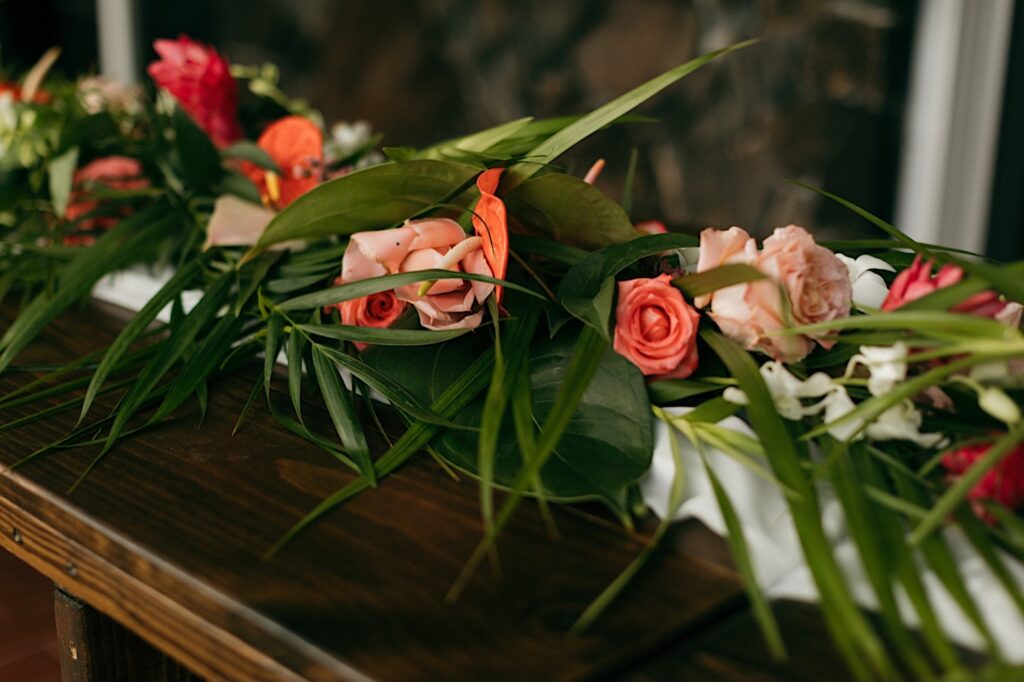 Pink flowers and green leaves sit on a table as decorations for a wedding
