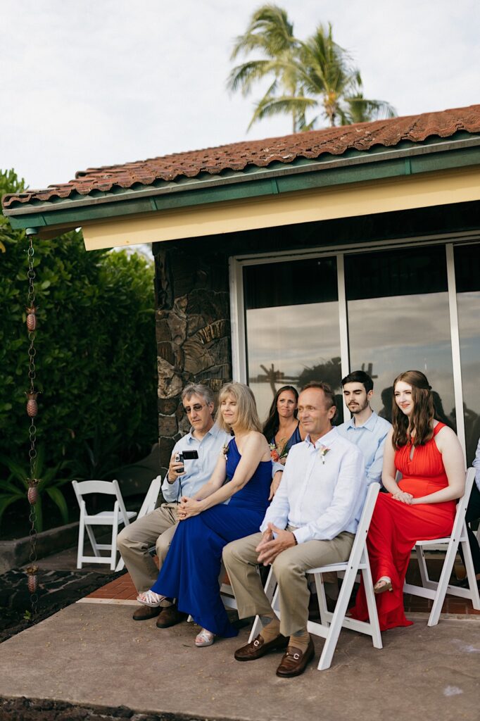 Guests of a wedding ceremony sit in chairs in a backyard on a patio
