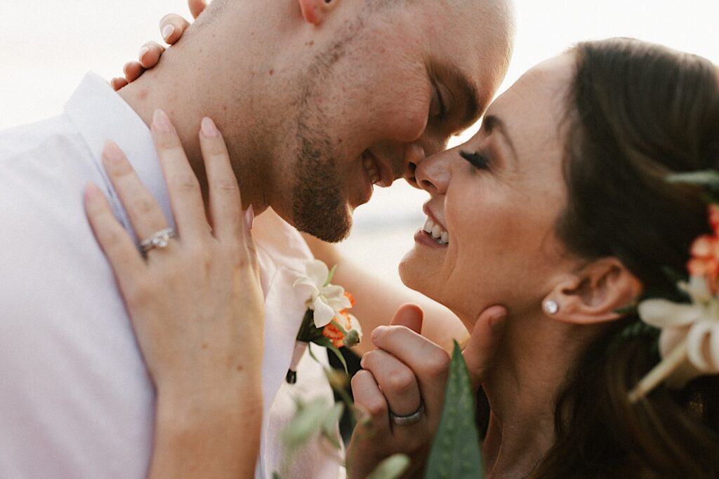 Close up photo of a bride and groom about to kiss one another and smiling with their wedding rings on display