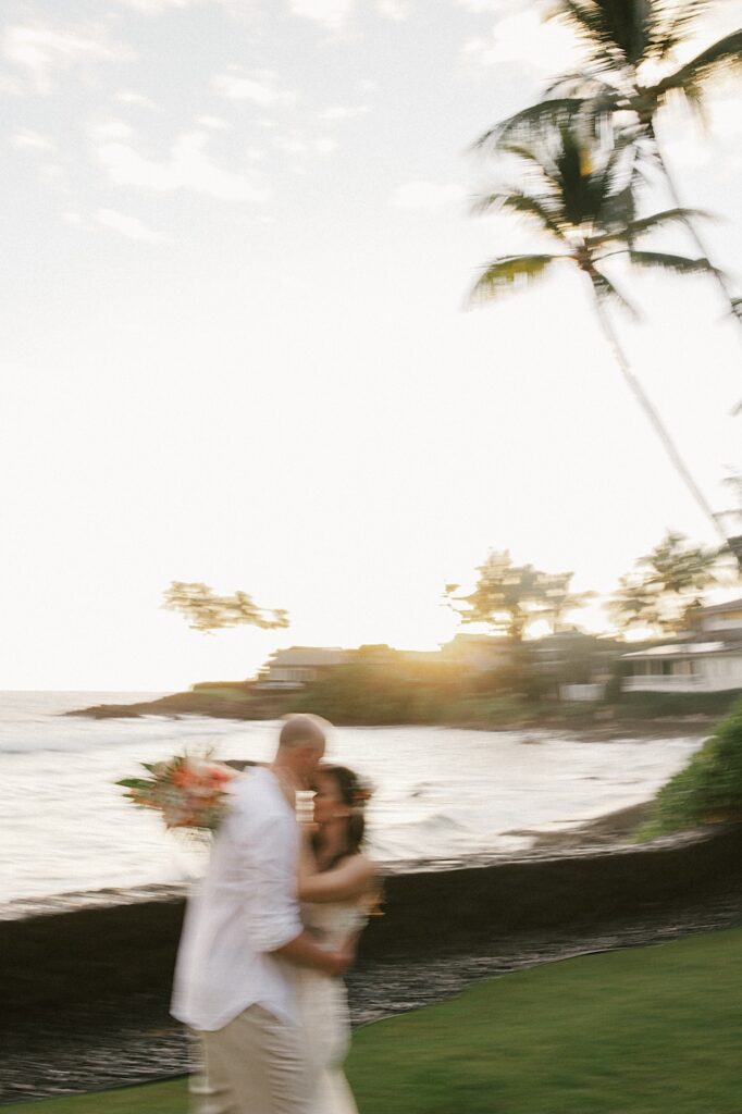Blurry photo of a bride and groom embracing while standing in backyard with the sun setting on the ocean behind them