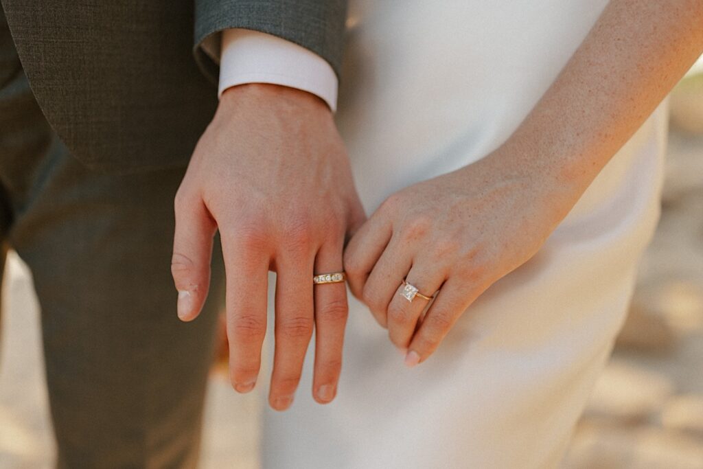 Close up photo of a bride and groom's hands holding one another, each wearing a wedding ring