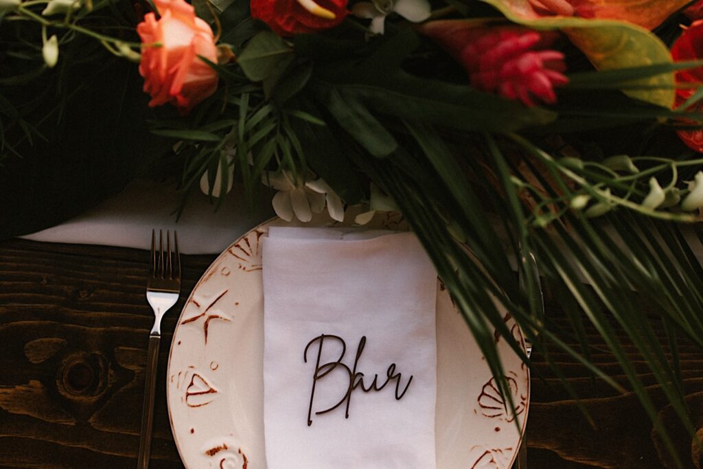 A napkin with the name "Blair" sits on a plate next to a fork with flowers and leaves on the table in front of it