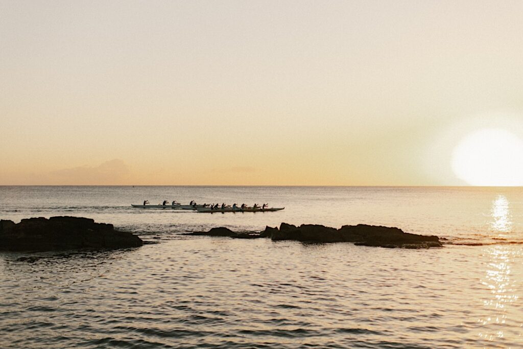 A couple of kayaks paddle along in the ocean in Hawaii as the sun sets behind them