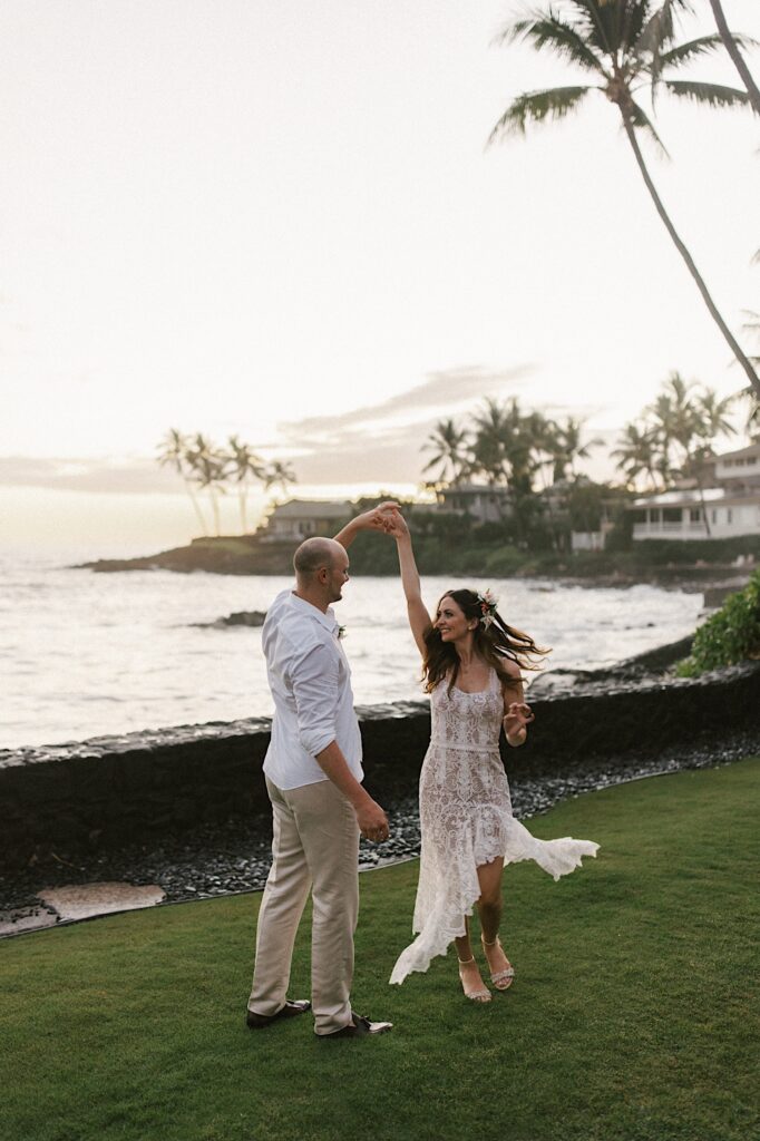 A bride and groom dance together in a backyard with the ocean and palm trees behind them