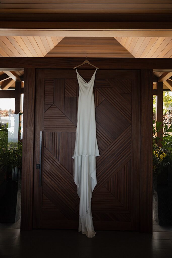 A wedding dress hangs from the ceiling in front of a wooden door