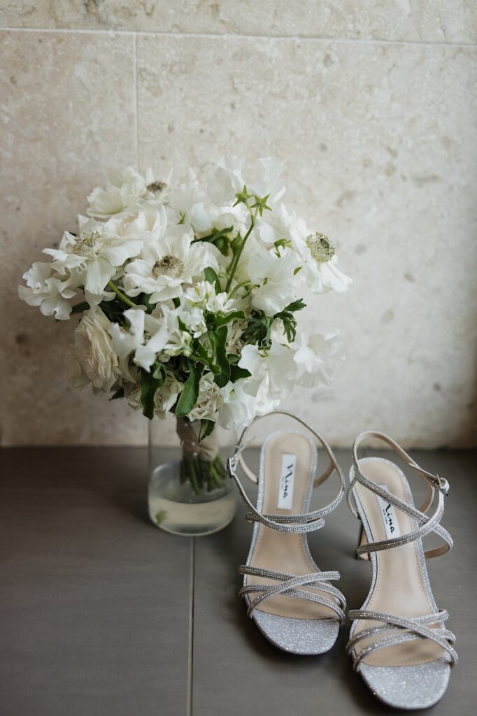Flowers in a vase sit on the floor next to a pair of women's shoes