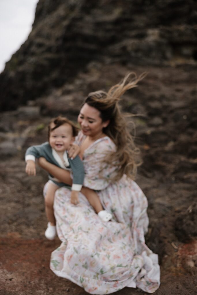 Out of focus photo of a smiling child sitting on the lap of their mother with a large rock formation behind them